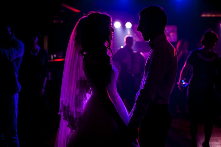 Romantic couple of newlyweds silhouettes posing at wedding reception surrounded by purple lights - GC Events Derby